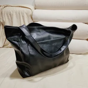 Primer plano de bolso tote negro de piel suave encerada con bolsillo y bandolera.