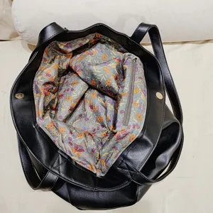 Vista interior detallada del bolso tote de cuero negro con forro floral de colores vivos