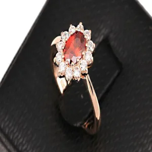 Close-up of elegant rose gold ring featuring an oval red zircon and white halo.