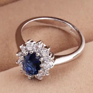 Close-up view of silver-tone ring featuring oval blue stone and halo of clear crystals.