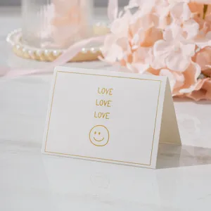 Detalle de pequeña tarjeta de felicitación blanca con texto LOVE dorado y una cara