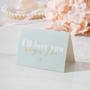 Primer plano de tarjeta de felicitación azul con corazón y texto romántico en oro.