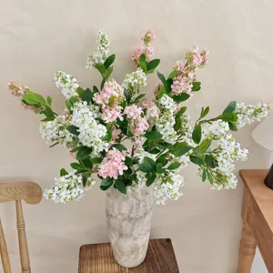 Detailed view of artificial pink and white lilac flowers in a textured stone vase.