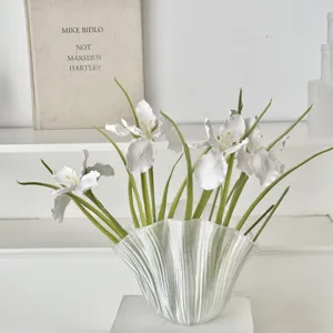 Elegant white artificial iris flowers in a pleated glass vase for minimalist home decor.