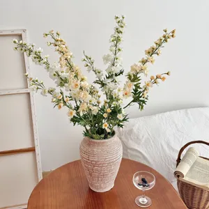 Elegant artificial delphinium flowers in a textured ceramic vase on a wooden table decor
