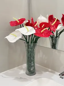 Vibrant red and white EVA artificial Anthurium flowers in a glass vase on a vanity.