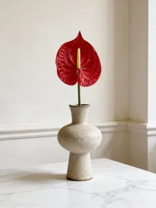Close-up of a vibrant red artificial anthurium flower in a minimalist ceramic vase