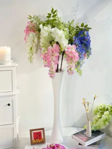 Üppige künstliche Blauregenblüten in einer minimalistischen hohen weißen Keramikvase