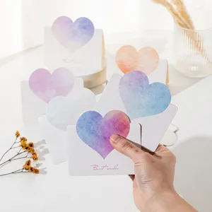 Hand holding several heart-shaped greeting cards with gradient colors and Best Wishes text.