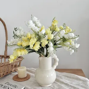 Elegant künstliche Maiglöckchen in Gelb und Weiß in einer cremefarbenen Keramikvase