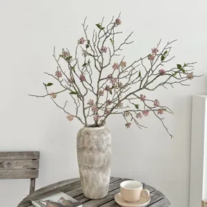 Λεπτομερής λήψη τεχνητών κλαδιών στυλ wabi-sabi με ροζ άνθη σε ένα όμορφο ρουστίκ βάζο