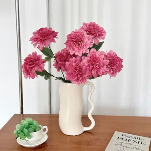 Detail of realistic pink dahlia artificial flowers in a modern white ceramic vase on wood table