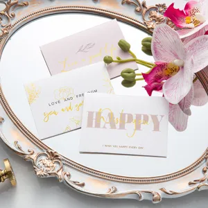 Elegantes tarjetas de felicitación con pan de oro en bandeja de espejo y flores.