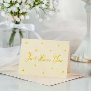 Detalle de tarjeta de felicitación crema con texto Just Love You en pan de oro y corazones