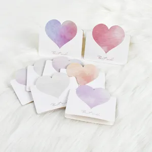 Close-up detail of pastel watercolor heart greeting cards on white faux fur background.