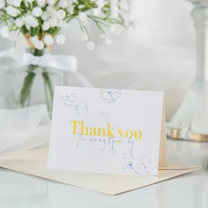 Detalle de una elegante tarjeta de agradecimiento floral blanca con letras doradas.