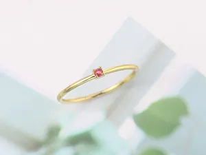 Primer plano detallado de un anillo fino minimalista con circón rosa en baño de oro claro.