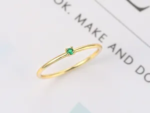 Detalle macro de un anillo minimalista bañado en oro con una piedra de circón verde