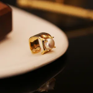 Close-up of a minimalist gold square ear cuff with a single large white pearl detail.