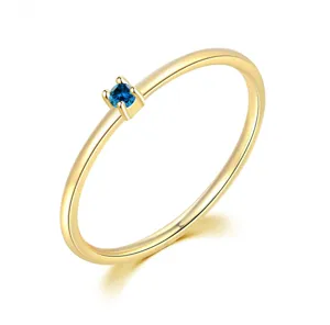 Detalle de un anillo minimalista chapado en oro con una pequeña piedra de circonita azul