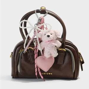 Brown leather handbag featuring a cute pink plush bear keychain and pearl bow charms.