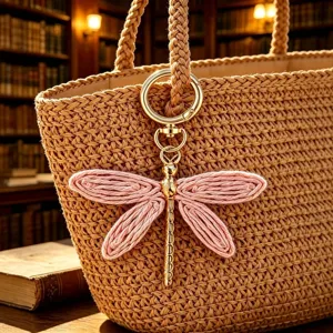 Primo piano del ciondolo portachiavi libellula rosa intrecciato a mano con anello oro.
