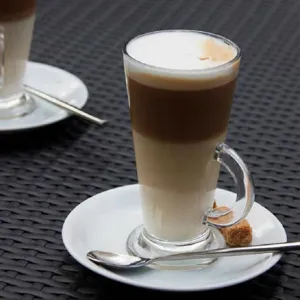 Clear glass coffee mug detail showing layered latte in a elegant handled cup with saucer.
