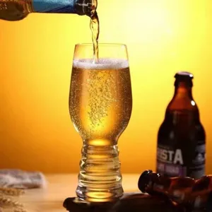 Primer plano de cerveza artesanal vertida en un vaso con base estriada y espuma dorada