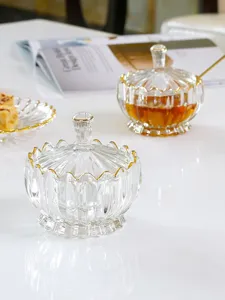 Nahaufnahme eines klaren Glasbonbonglases mit elegantem Goldrand und Deckel auf weißem Tisch