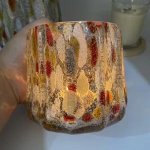 Handheld detailed view of handmade speckled glass candle holder with bubbles and colorful spots.