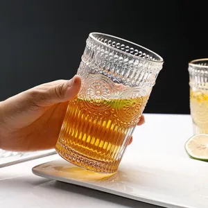 Detail of hand holding vintage sunflower embossed glass cup with gold rim