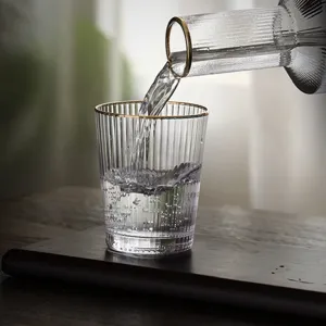 Detailed close-up showing water pouring into a fluted glass with a gold rim on a dark wood board.