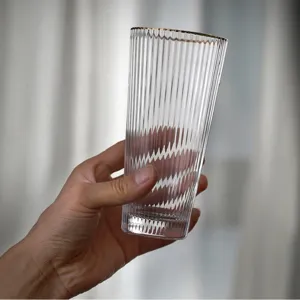 Close-up of a vintage ribbed glass cup with an elegant gold rim held in a person's hand