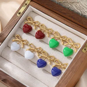 Close-up of colorful bowknot heart enamel earrings displayed in a wooden jewelry box.