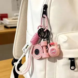 Detailed closeup of cute pink gym keychain with dumbbell and kettlebell charms on white backpack.