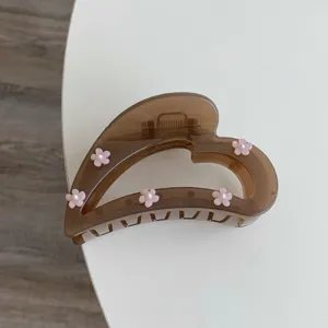 Detailaufnahme einer braunen herzförmigen Haarklammer mit rosa Blüten und Perlenverzierung.