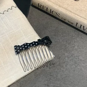 Macro view showing the fine details of a black acetate polka dot bow hair comb accessory.