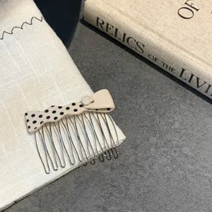 Close-up detail of a cream acetate hair comb featuring a stylish black polka dot bow