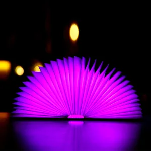 Faltbare Holzbuchlampe mit lila LED-Licht, fächerförmig auf dunklem Hintergrund