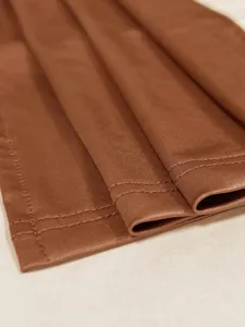 Detailansicht eines braunen figurbetonten Kleides mit hochwertigen Nähten und glatter Textur.