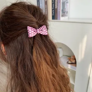 Detail view of a pink polka dot bow acetate hair clip styled on long wavy brown hair