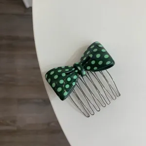 Detailed view of a dark green acetate bow hair comb featuring light green polka dots.