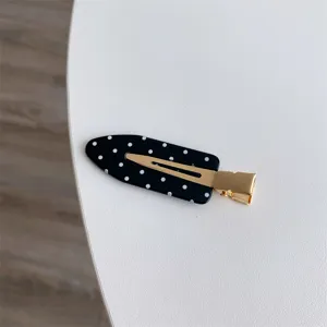 High-quality detail shot of a black hair clip with white polka dots and gold clip