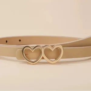 Close-up detail of the elegant gold double heart buckle on a minimalist beige leather belt.