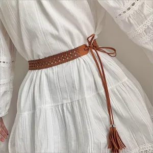 Dettaglio di una cintura in pelle intrecciata marrone con nappe su abito bianco chic.