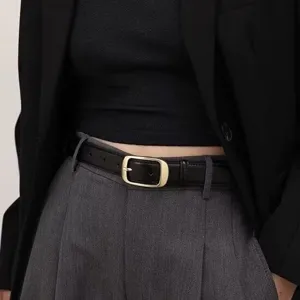 Dettaglio di una cintura in pelle nera minimalista con elegante fibbia rettangolare.