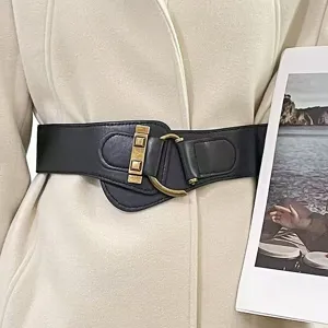 Dettaglio di un'ampia cintura elastica nera con fibbia dorata su cappotto beige