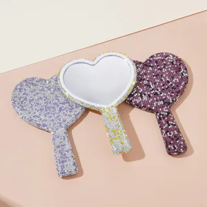 Close-up of heart-shaped handheld makeup mirror with sparkling rhinestones and elegant handle.