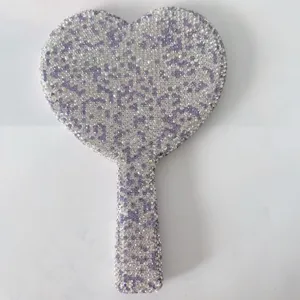 Close-up of a cute heart-shaped rhinestone handheld makeup mirror with glittering crystal gems.