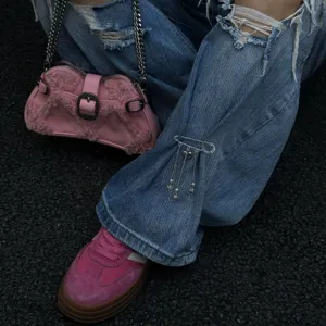 Spilla da balia trendy Y2K con catena a cuore e croce su dei jeans blu strappati